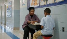 Tutor sitting with student in school hall